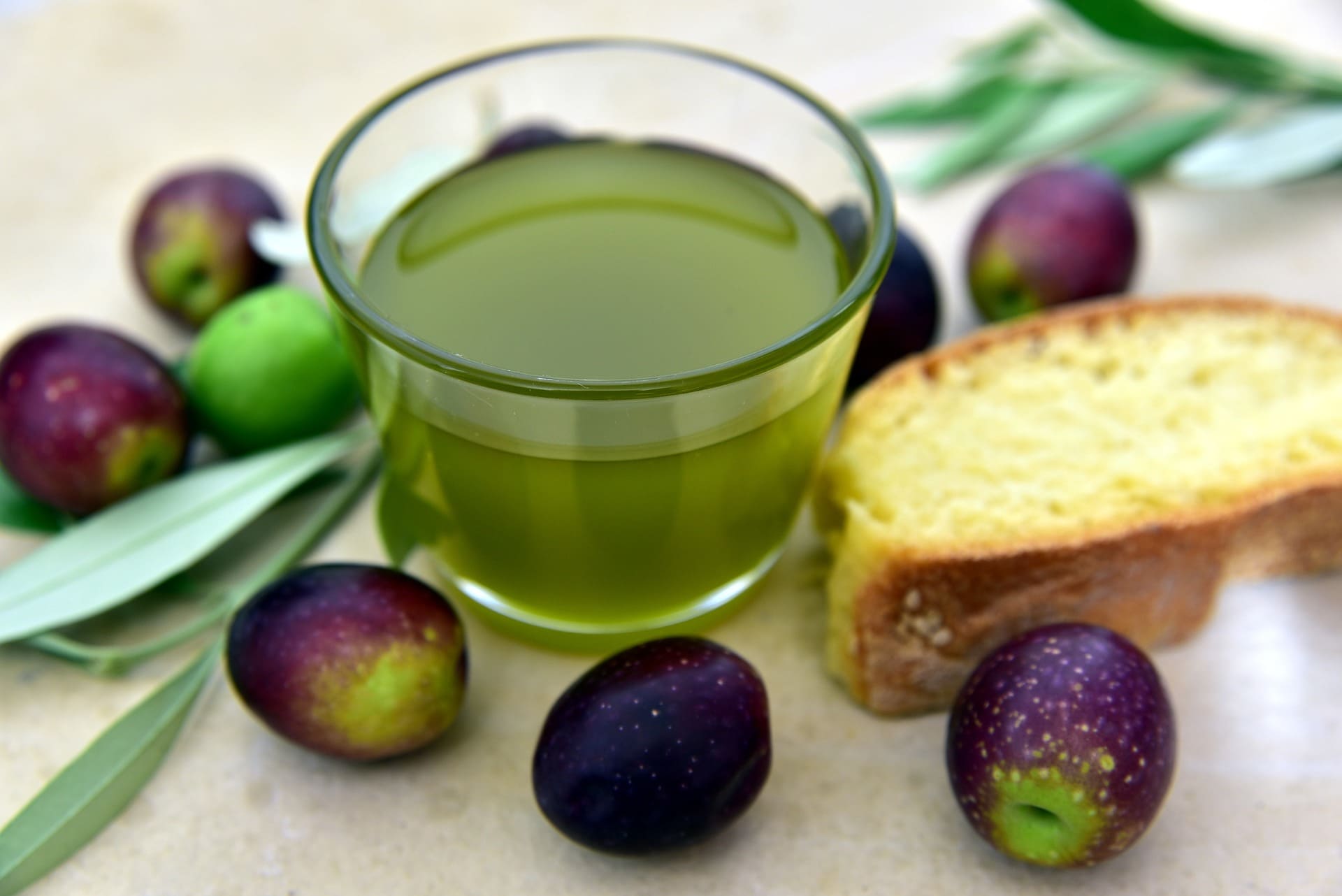 bicchiere d'olio nuovo con delle olive ed una fetta di pane